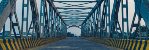 Blick auf eine lange Brücke, die sich in der Ferne bis zum Horizont erstreckt. Der Betrachter steht am Anfang der Brücke und schaut in die Weite, wobei die Struktur der Brücke deutlich sichtbar ist und den Weg bis zum Ende führt.